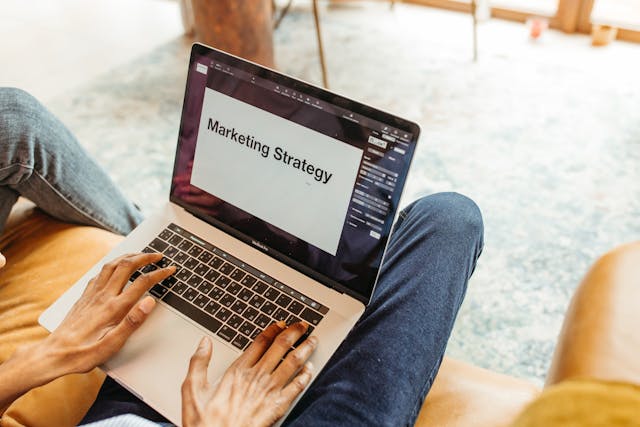 someone sitting on a yellow couch with an open laptop that reads "marketing strategy"