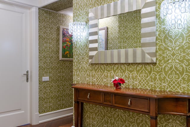 A hallway with green patterned wallpaper and a mirror.