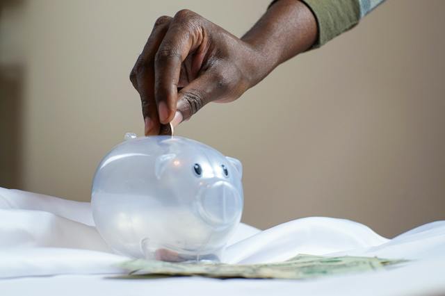 A hand depositing a coin into a piggybank.